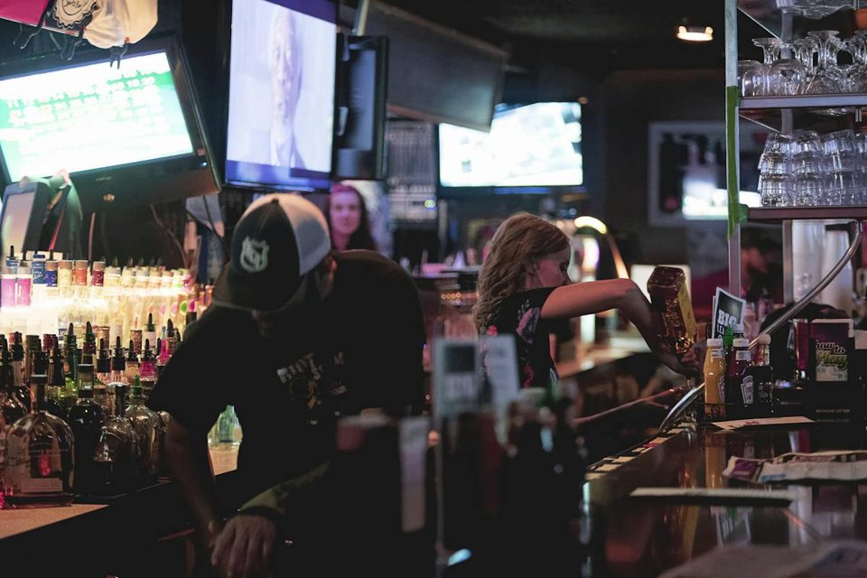 Bartenders at work behind the crowded bar, with TVs above them