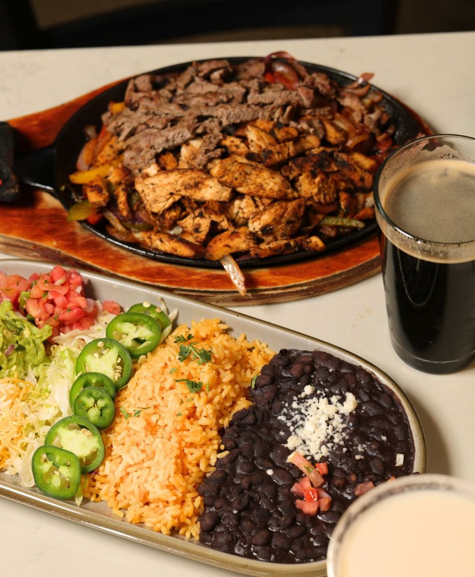 Fajitas öntöttvas serpenyőben marha- és csirkehússal, mellette rizs, fekete bab, jalapeño és egy pohár sötét sör