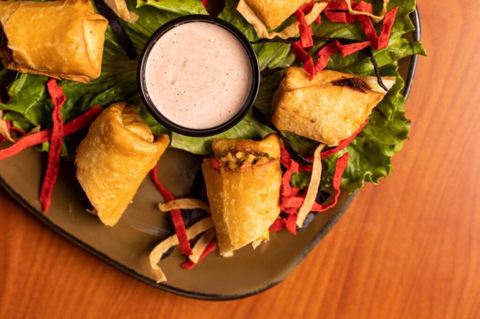 Crispy fried rolls on a bed of lettuce with tortilla strips and a small cup of dipping sauce