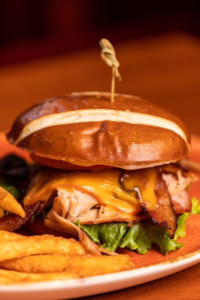 A pretzel-bun sandwich with sliced turkey, melted cheddar, bacon and lettuce, with fries on the side