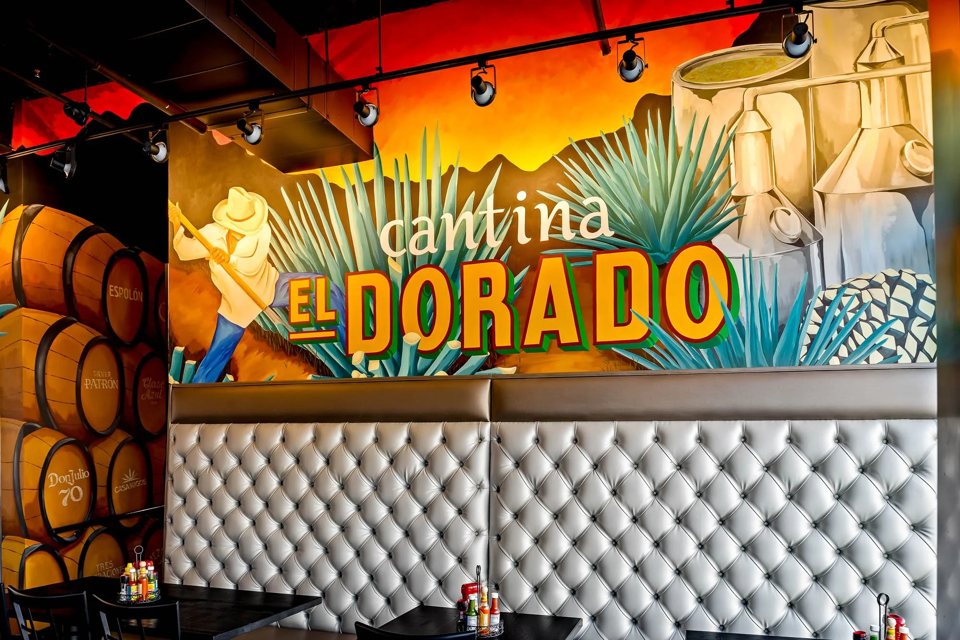 A mural with the place's name above a white tufted booth and barrels