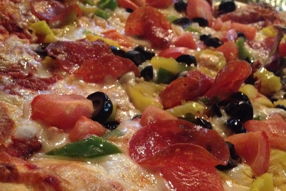 Közeli kép egy szalámis, olívabogyós, paradicsomos pizzáról