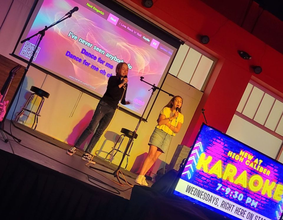Two singers on the karaoke stage with song lyrics projected on the screen behind them