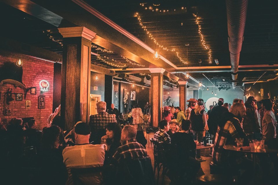 A crowded bar room with brick walls, wooden columns and string lights across the ceiling