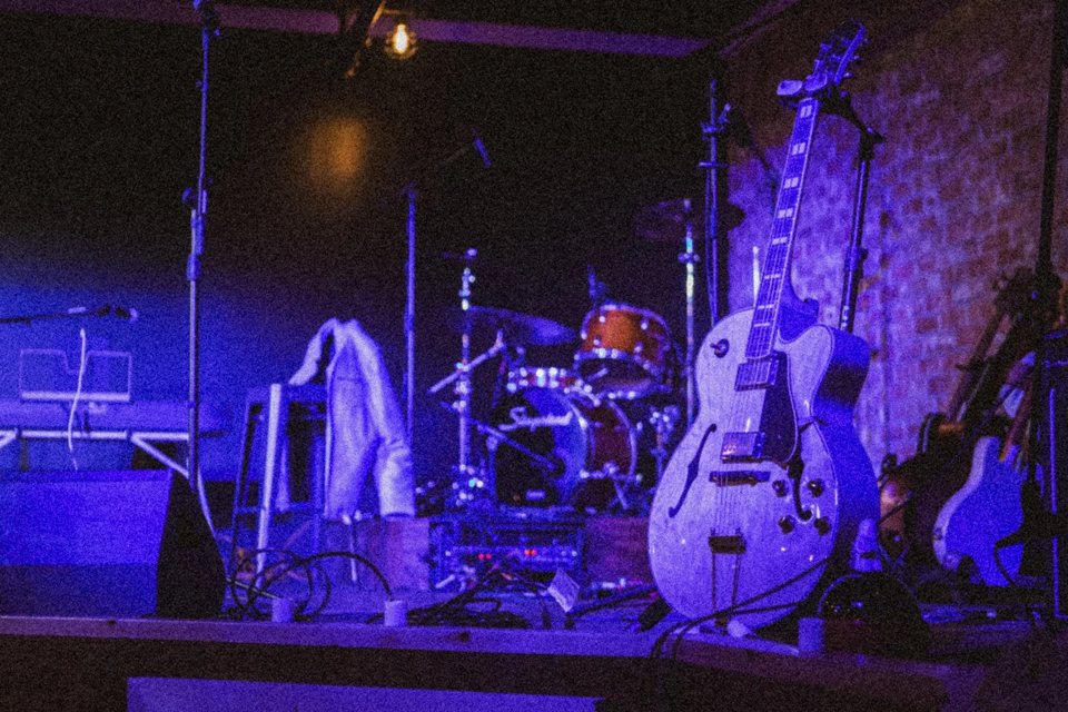 An empty stage in purple light with a drum kit, guitars and mic stands
