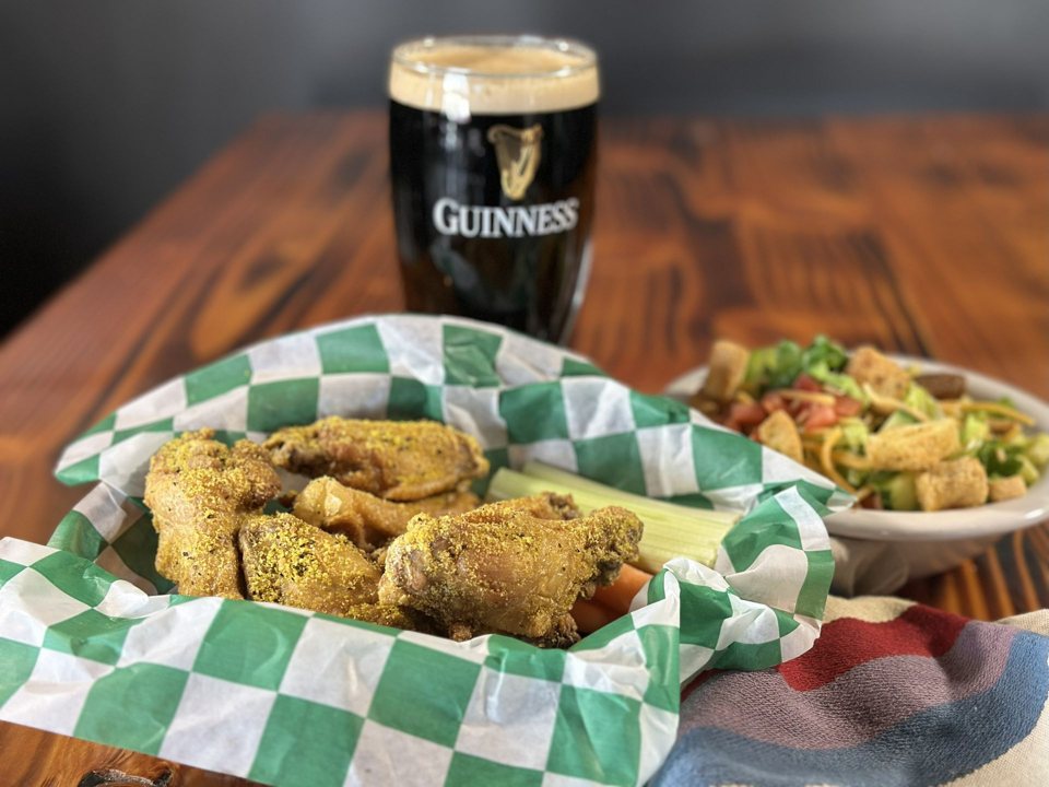 Fűszeres sült csirkefalatok kockás papírral bélelt kosárban, mögöttük egy pohár Guinness
