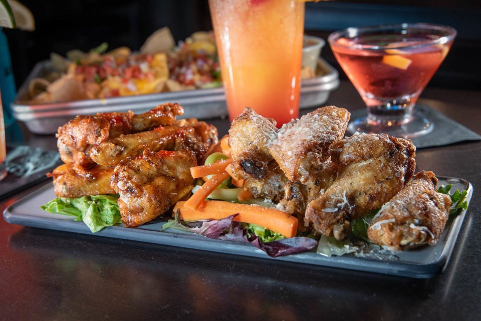 Chicken wings and fried bites on a platter with cocktails on the bar