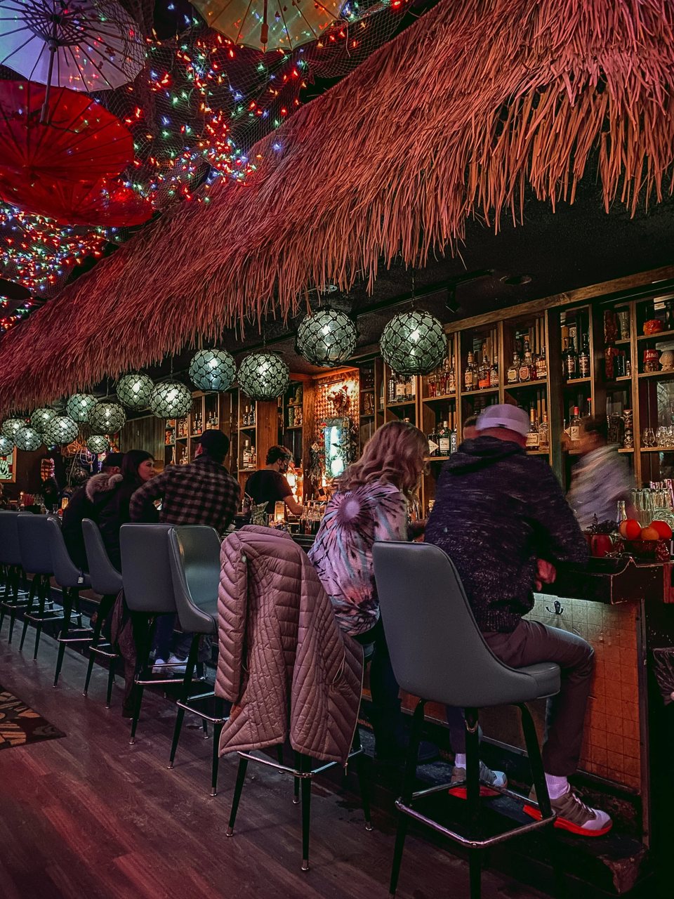 Guests at the bar under a thatched roof, paper umbrellas and string lights