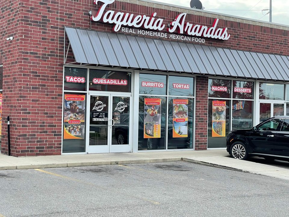 A brick building with a Taqueria Arandas sign, a metal awning and food posters in the windows