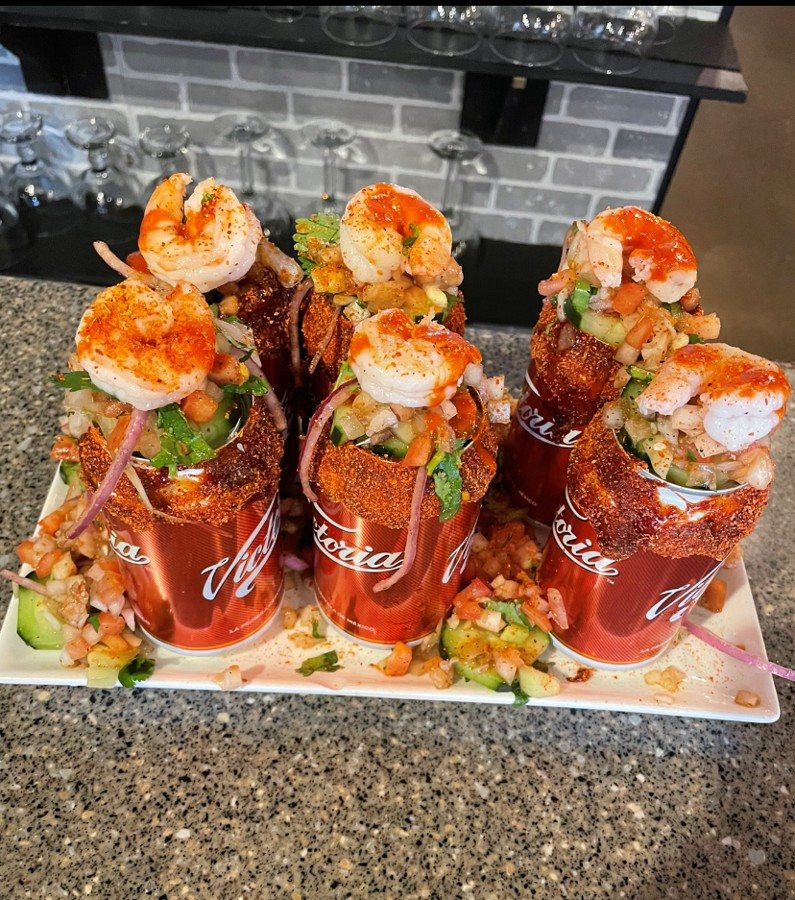 Shrimp and vegetable cocktails served in chili-rimmed beer cans on a plate on the counter
