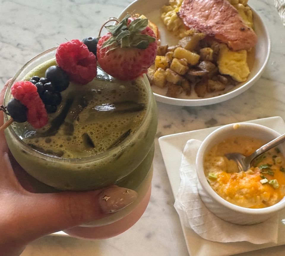 Green smoothie garnished with berries, with breakfast dishes behind