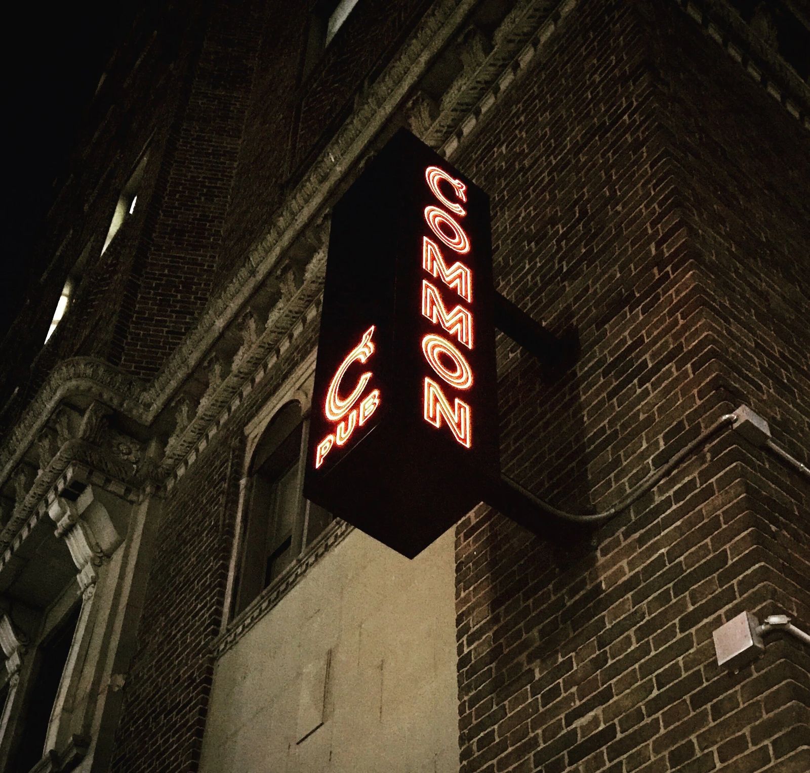 A Common Pub világító neonfelirata a téglaépület sarkán, éjjel