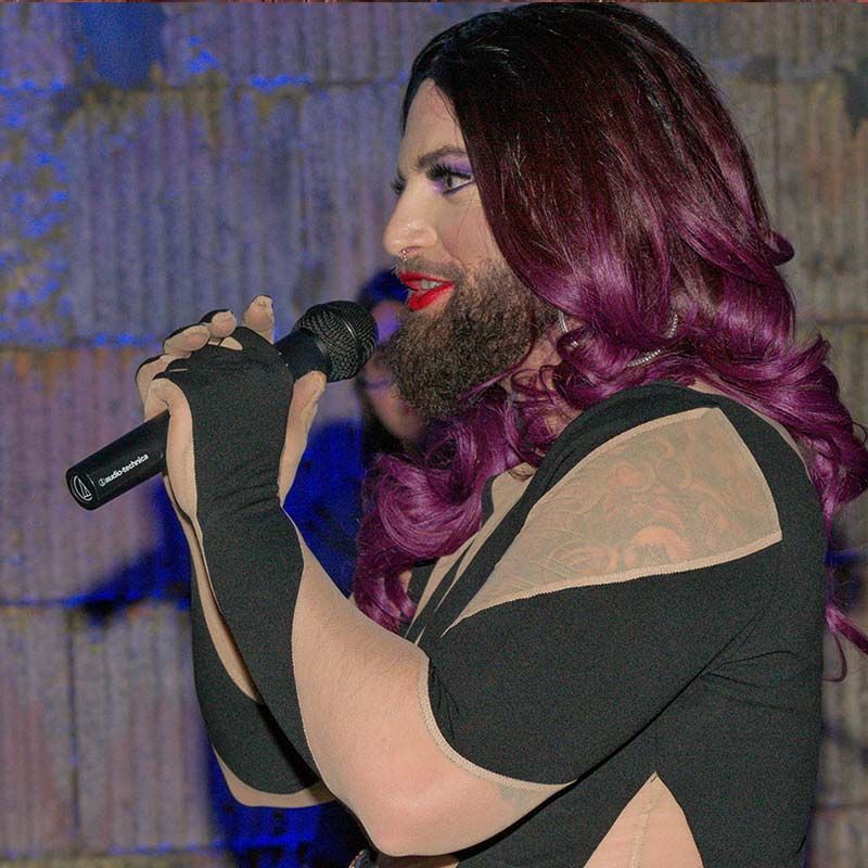 Lila hajú drag-előadó mikrofonba énekel