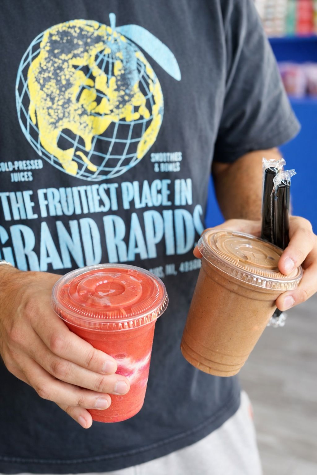 Két smoothie kézben, „The Fruitiest Place in Grand Rapids” feliratú póló előtt