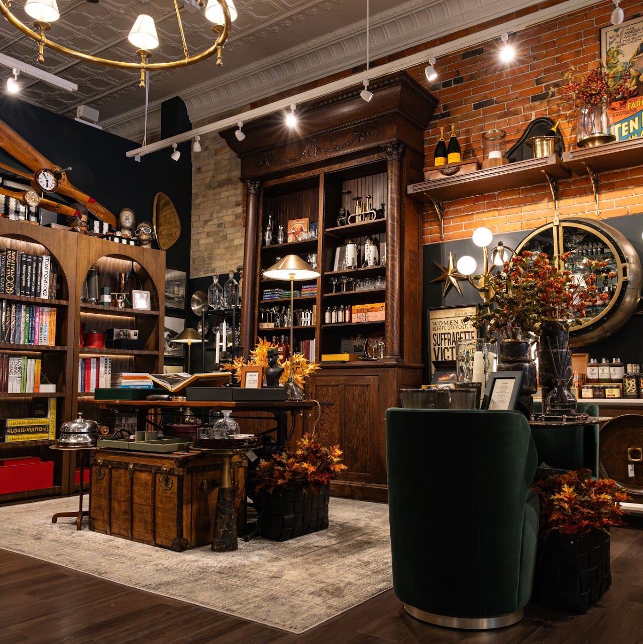 Wood-paneled shop interior with bookshelves, chandeliers and a green velvet armchair