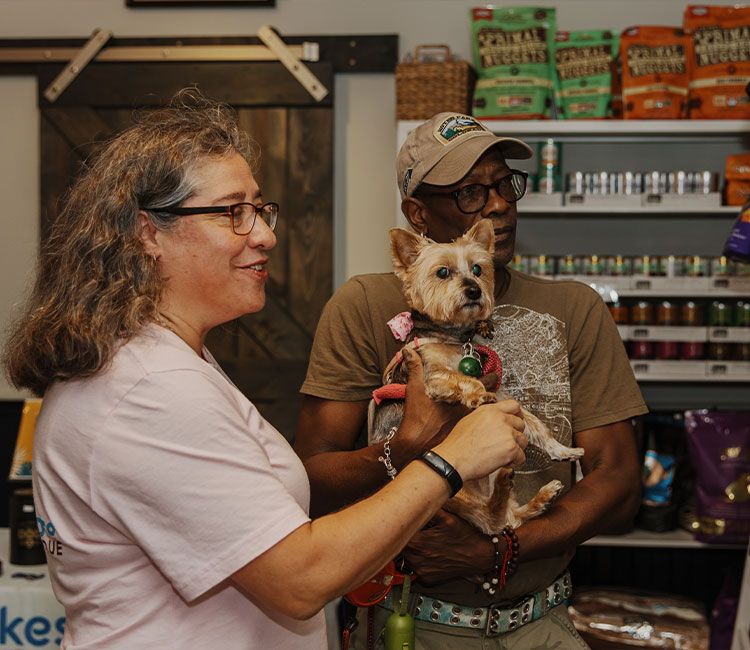 Shoppers holding a Yorkshire terrier among shelves of pet food