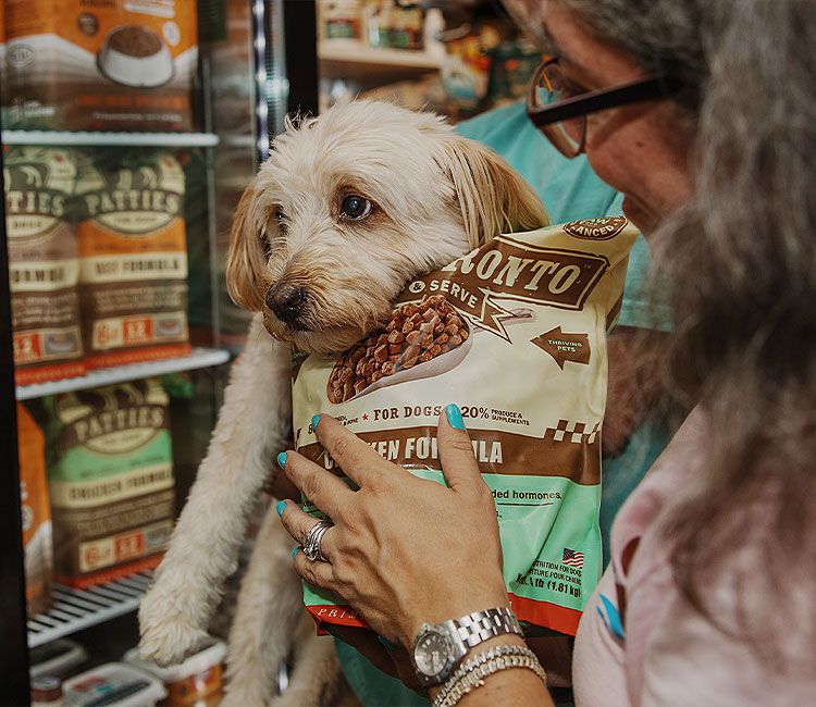 Small white dog beside a bag of dog food in front of the frozen food case