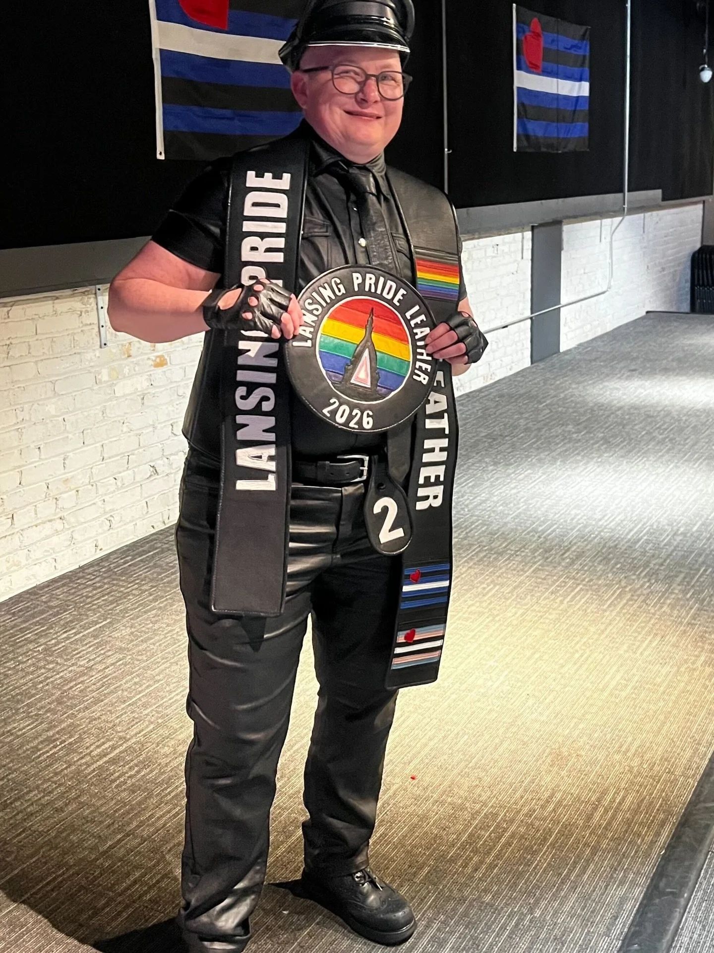 Bőrruhás résztvevő Lansing Pride Leather 2026 szalaggal és érmével