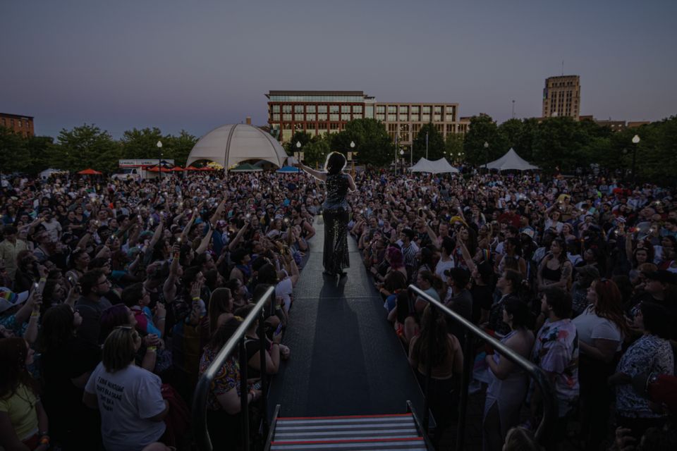 Performer on a runway before a huge crowd at an outdoor evening event