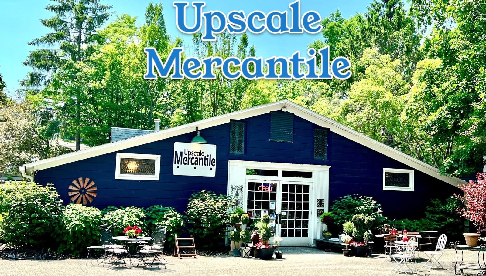 Upscale Mercantile's navy barn-style shop building among trees and flowers