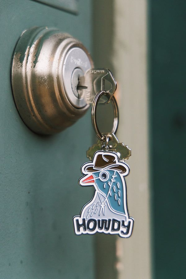 Kalapos madarat ábrázoló, „Howdy” feliratú kulcstartó egy ajtózárban