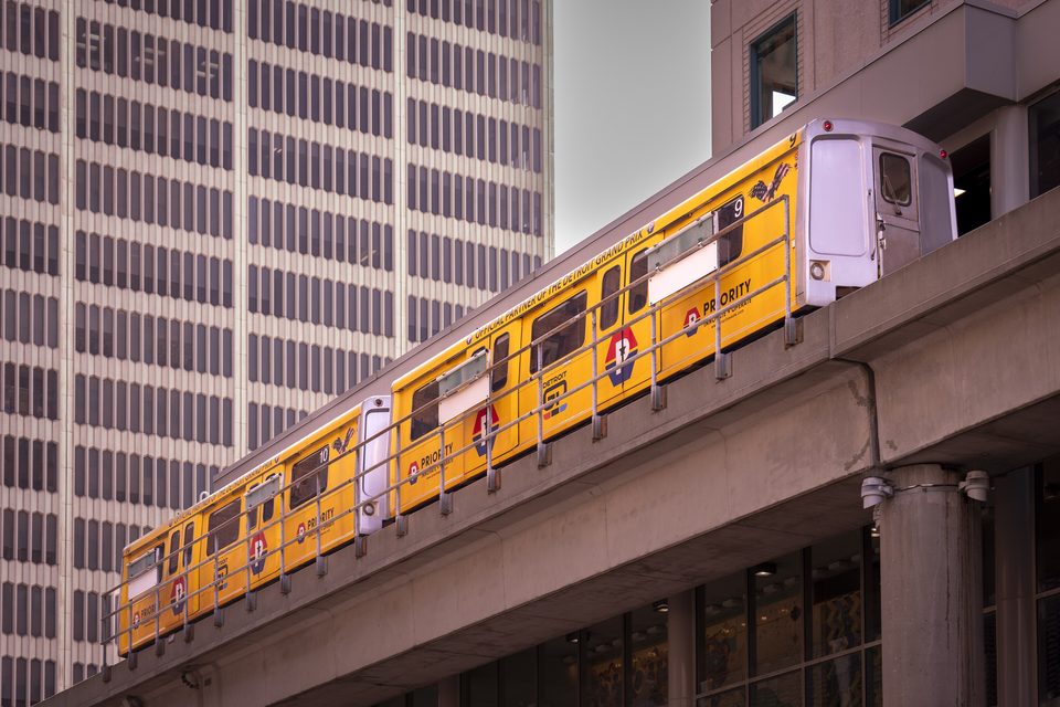 A yellow People Mover train on the elevated guideway in downtown Detroit (2024)