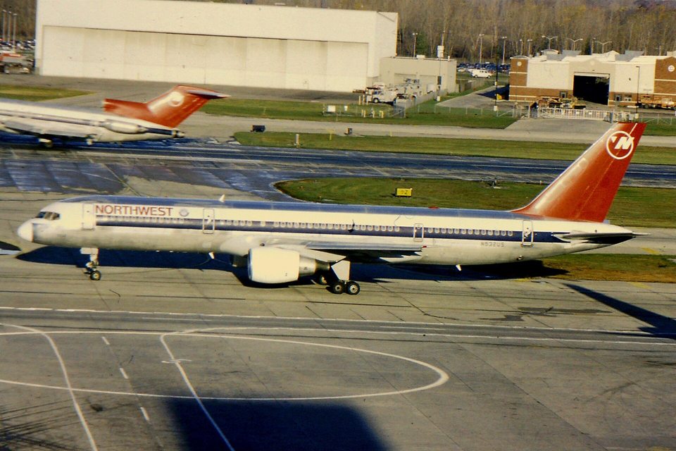 A Northwest Airlines piros farokfelületű Boeing 757-ese gurul a DTW-n 1994-ben, háttérben egy Northwest 727-es száll fel.