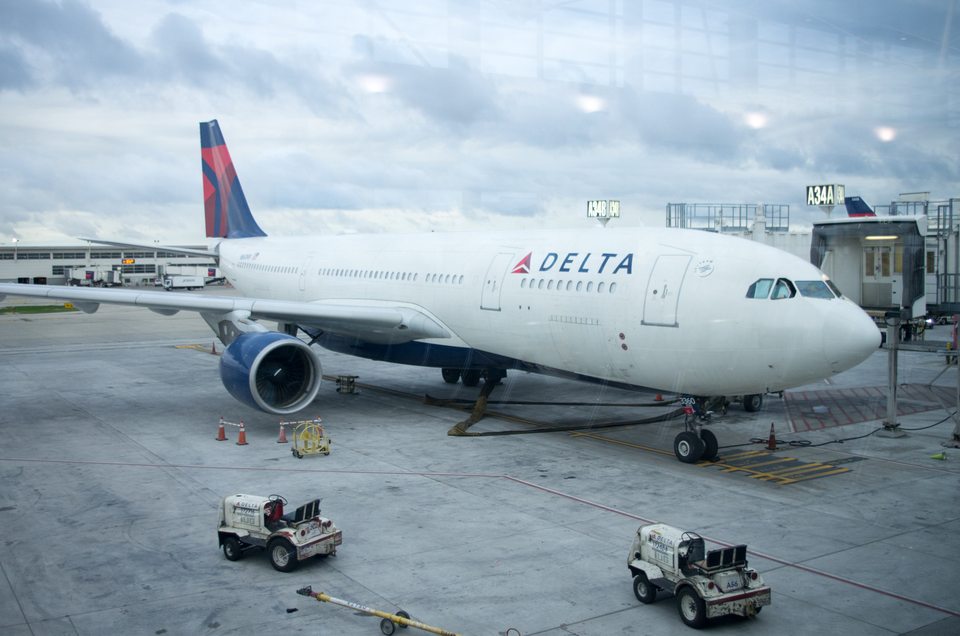 A Delta Air Lines Airbus A330-200-as gépe a McNamara terminál egyik kapujánál, a közelben földi kiszolgáló járművekkel.