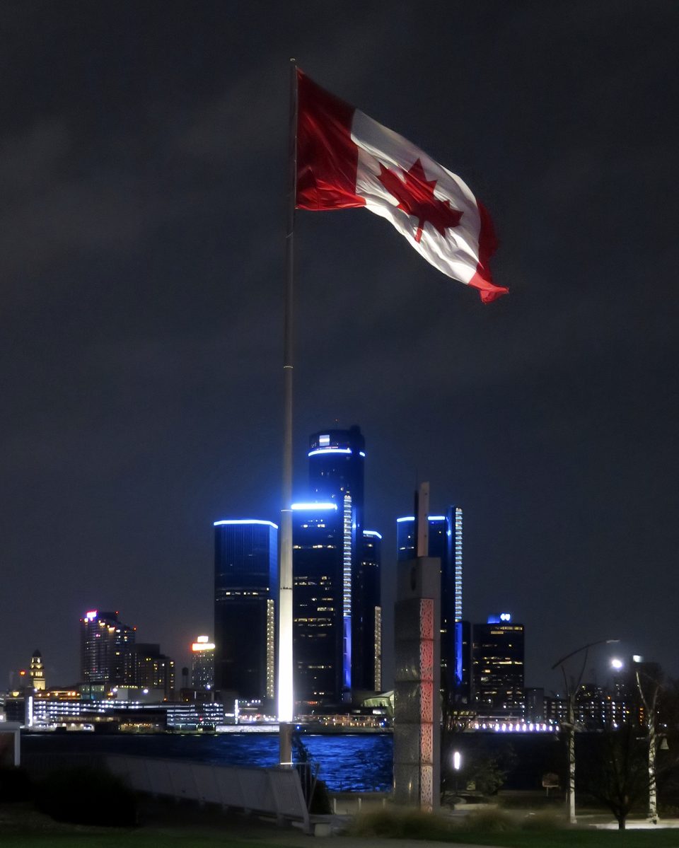A windsori Dieppe Gardens óriási kanadai zászlaja, a folyó túlpartján a kéken világító Renaissance Center (2022)