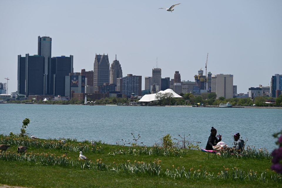Piknikezők a Belle Isle partján 2023 májusában, a folyó túloldalán a belváros, balra a Renaissance Center