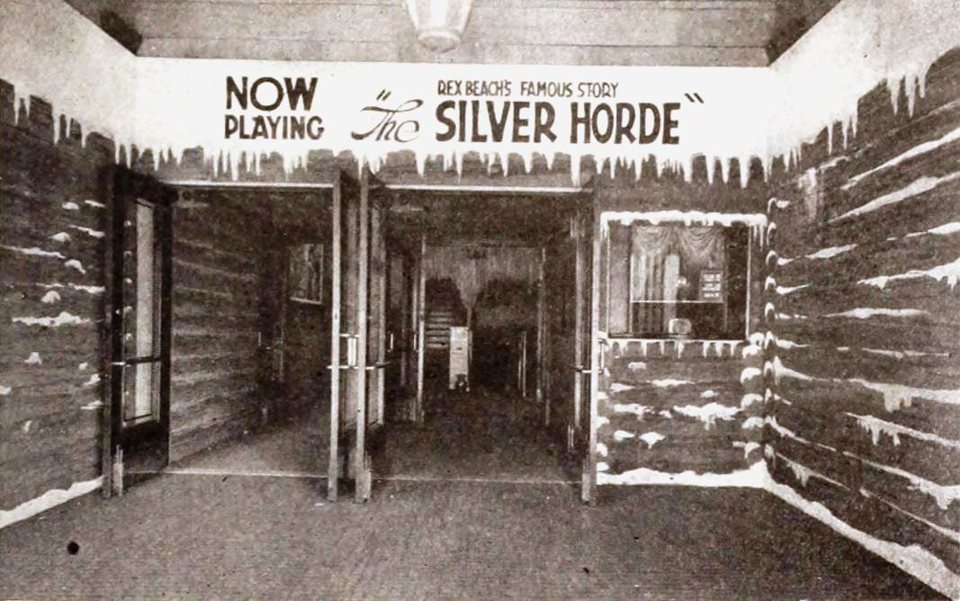 The Adams Theatre entrance in 1920, dressed up as a snowy log cabin for The Silver Horde, with a NOW PLAYING banner