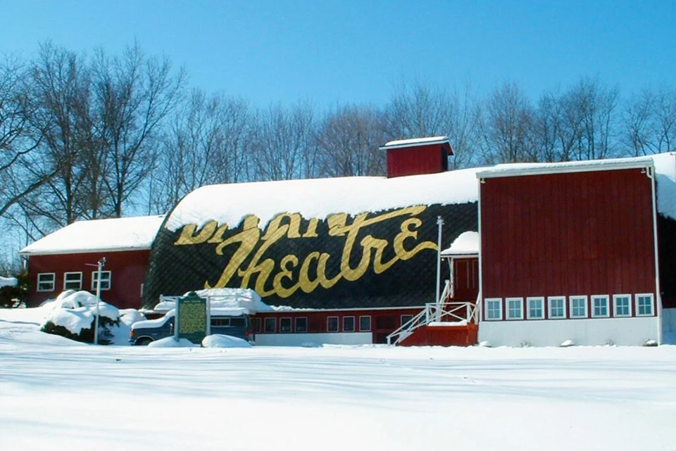 The red Barn Theatre barn in the snow, with the big gold Barn Theatre script across its roof under a blue sky