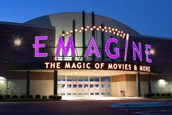 Az Emagine mozi kivilágított lila felirata és „The Magic of Movies & More” előtetője esti szürkületben