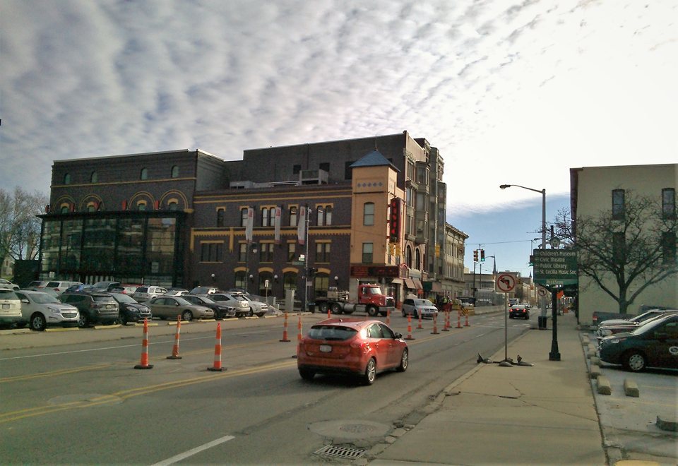 The Grand Rapids Civic Theatre's brick building with its vertical red sign on a downtown street, with parked cars and traffic cones in front