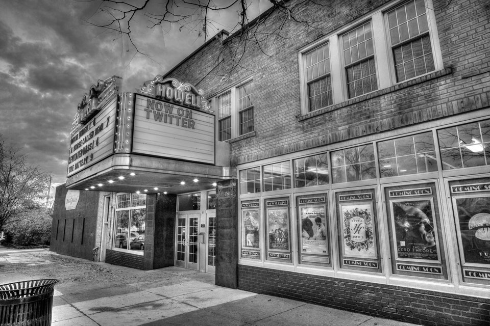Black-and-white photo of the Howell Theater marquee and its poster-filled display windows under a cloudy sky