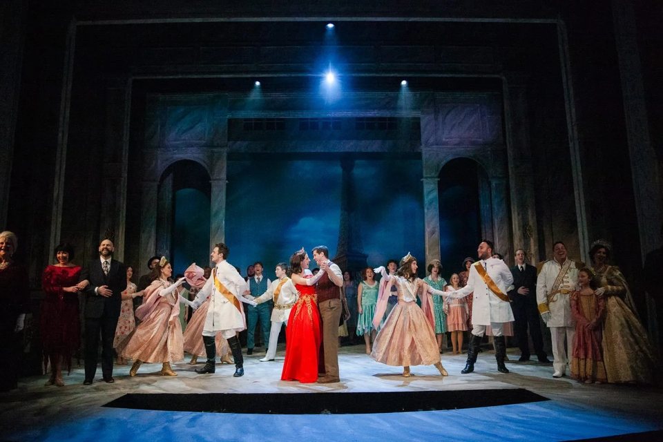 The ballroom scene of Anastasia, with the lead in a red gown and costumed couples before a Paris backdrop