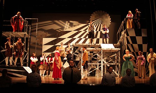 Actors in Renaissance costume on a multi-level black-and-white checkered set