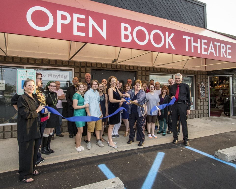 Ribbon-cutting under the red Open Book Theatre awning, with company members and supporters
