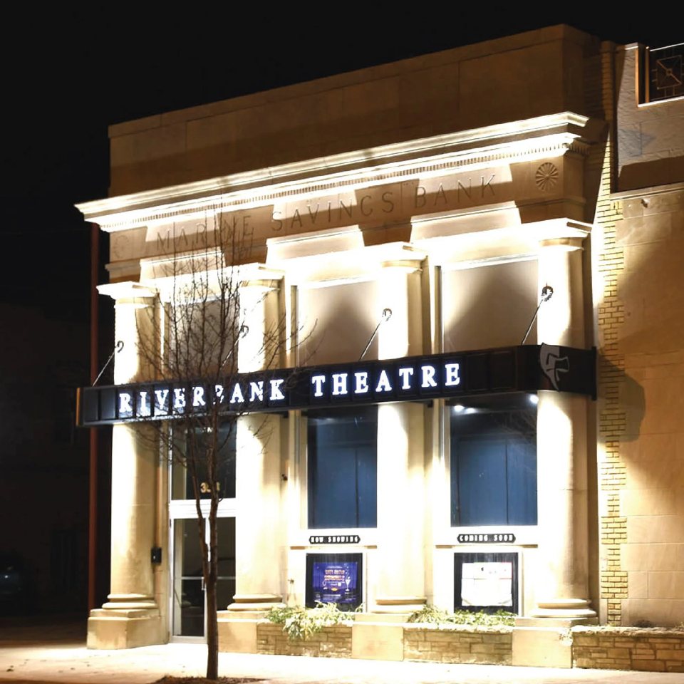 The Riverbank Theatre's lit, columned facade at night in the former Marine Savings Bank building
