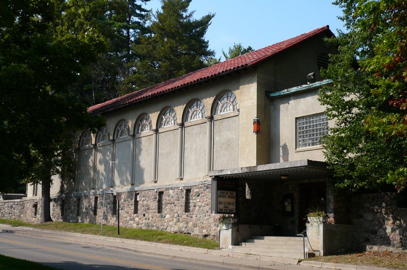 The theatre's stone-based building with a red tile roof and a row of arched windows among the trees