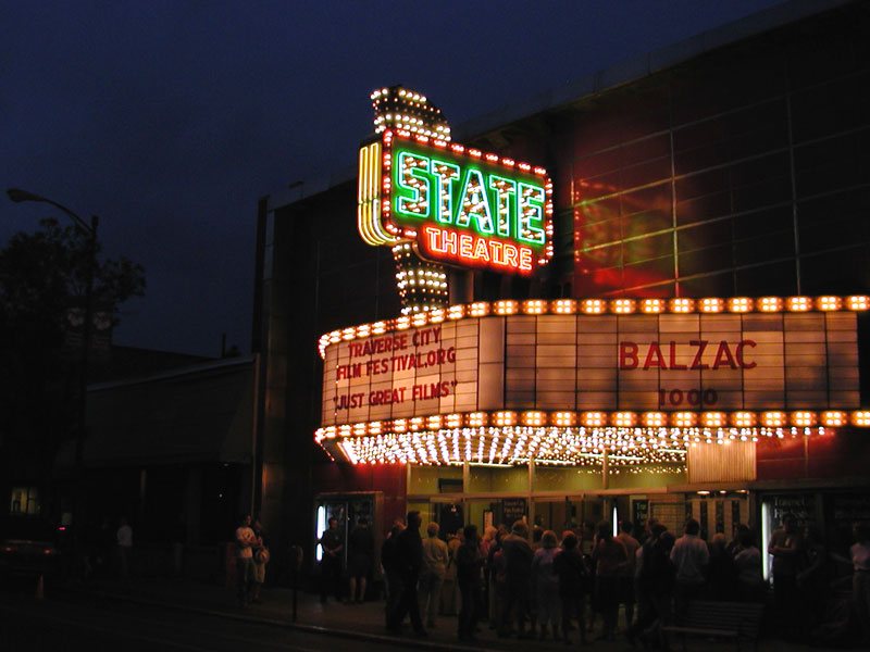 The lit STATE sign and marquee at night, with a crowd gathering below