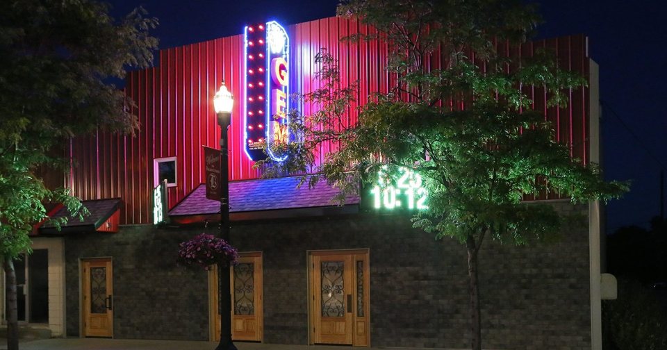 The vertical GEM neon sign glowing on the red metal facade at night, with trees and a street lamp in front