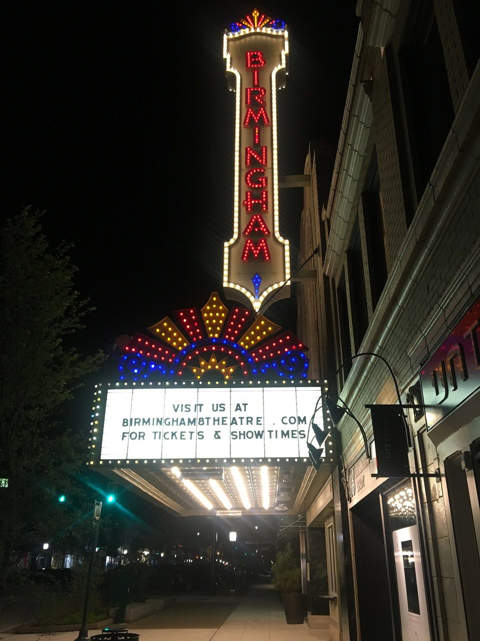 The lit vertical BIRMINGHAM sign and sunburst marquee over the sidewalk at night