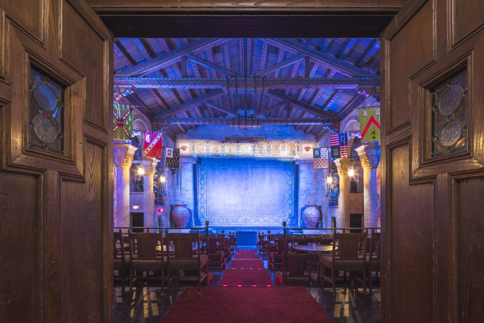 The blue-lit stage seen through open carved wooden doors, with a red-carpeted aisle leading down