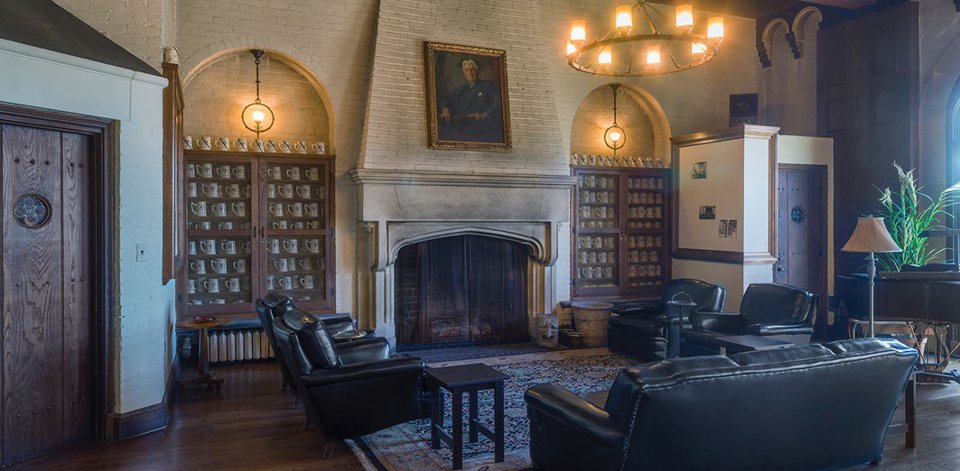 A lounge with a stone fireplace, leather armchairs, a chandelier and cabinets full of mugs