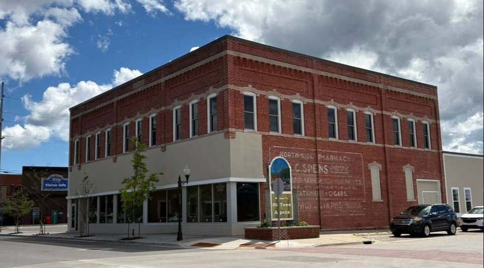 A two-story red brick corner building in Old Town Alpena, with a faded old pharmacy sign painted on its side
