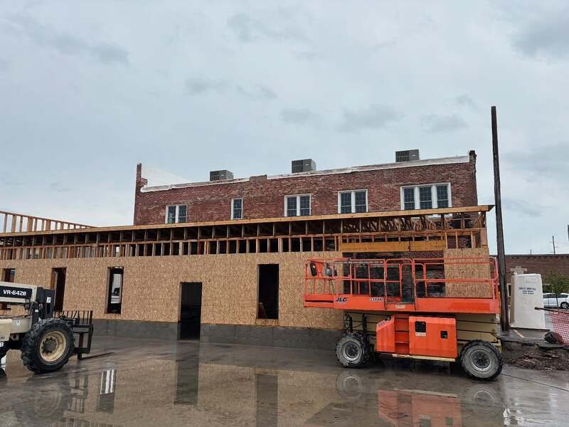 An addition under construction, with wood framing and a scissor lift beside the brick building