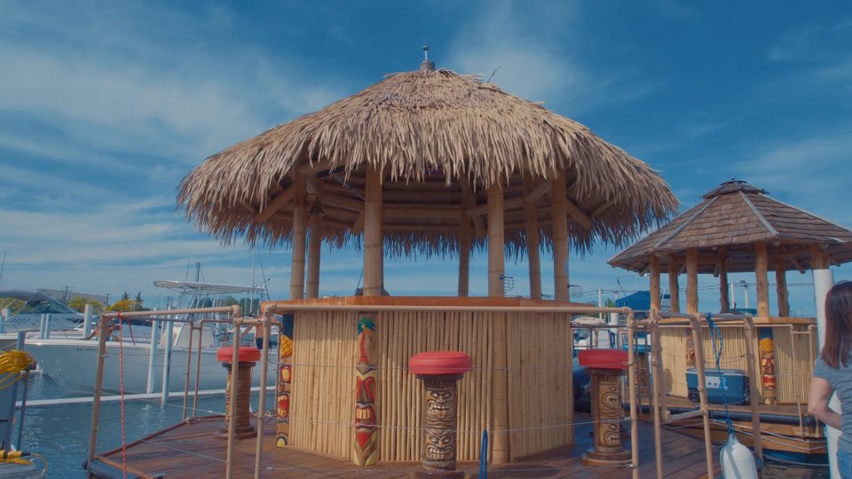 Szalmatetős tiki bárcsónakok kikötve a marinában, vitorlások a háttérben