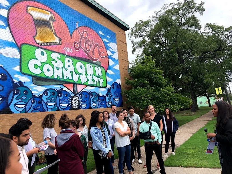 A tour group listens to the guide in front of a colorful community mural