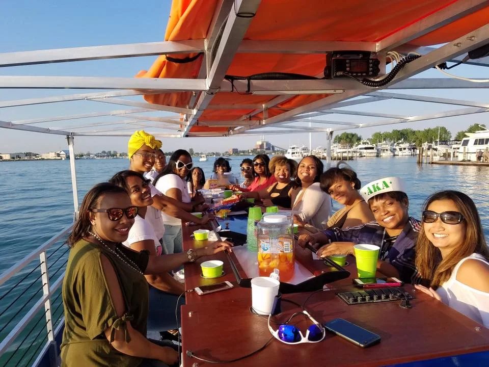 Vidám társaság ünnepel a Detroit Cycle Boat fedélzetén, mögötte a kikötő